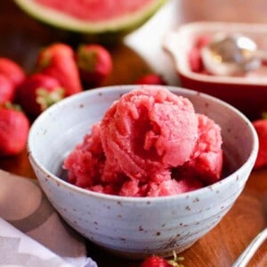 a blue bowl filled with watermelon sorbet surrounded by fresh strawberries on a wooden table