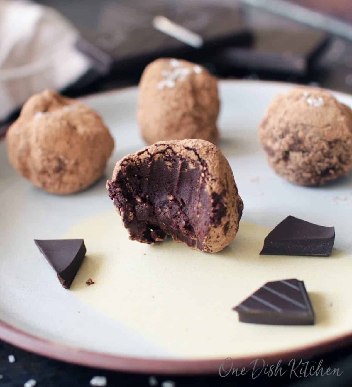 Four chocolate truffles coated in cocoa powder and one has a bite taken from it all on a plate