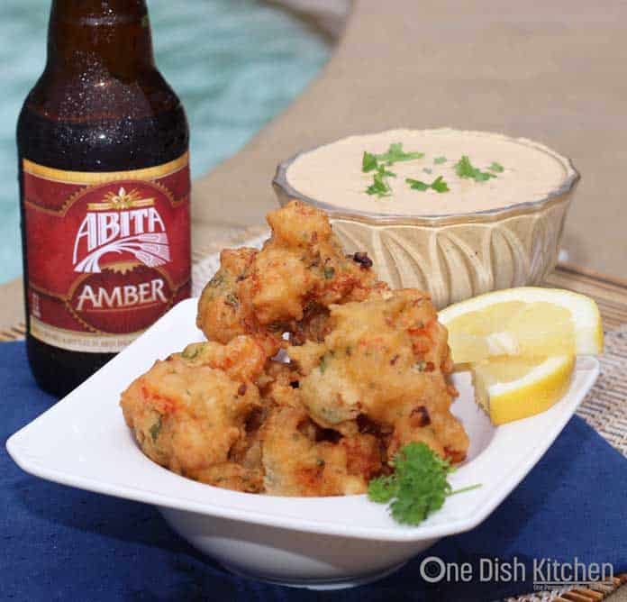 Crawfish Beignets in a bowl next to a bowl of Creamy Remoulade Sauce and a bottle of beer with a swimming pool in the background.