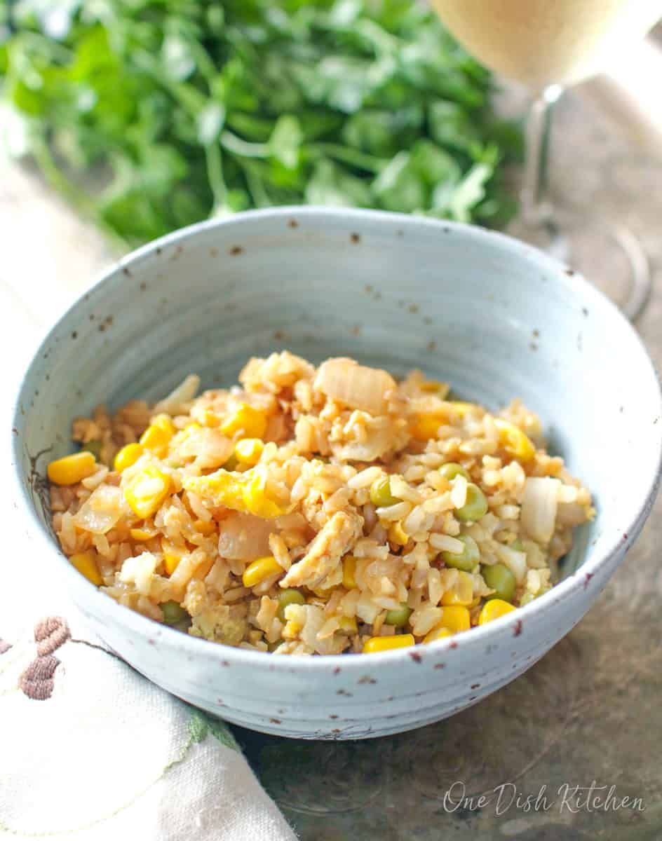 a blue bowl filled with fried rice, corn and peas next to a bunch of parsley.