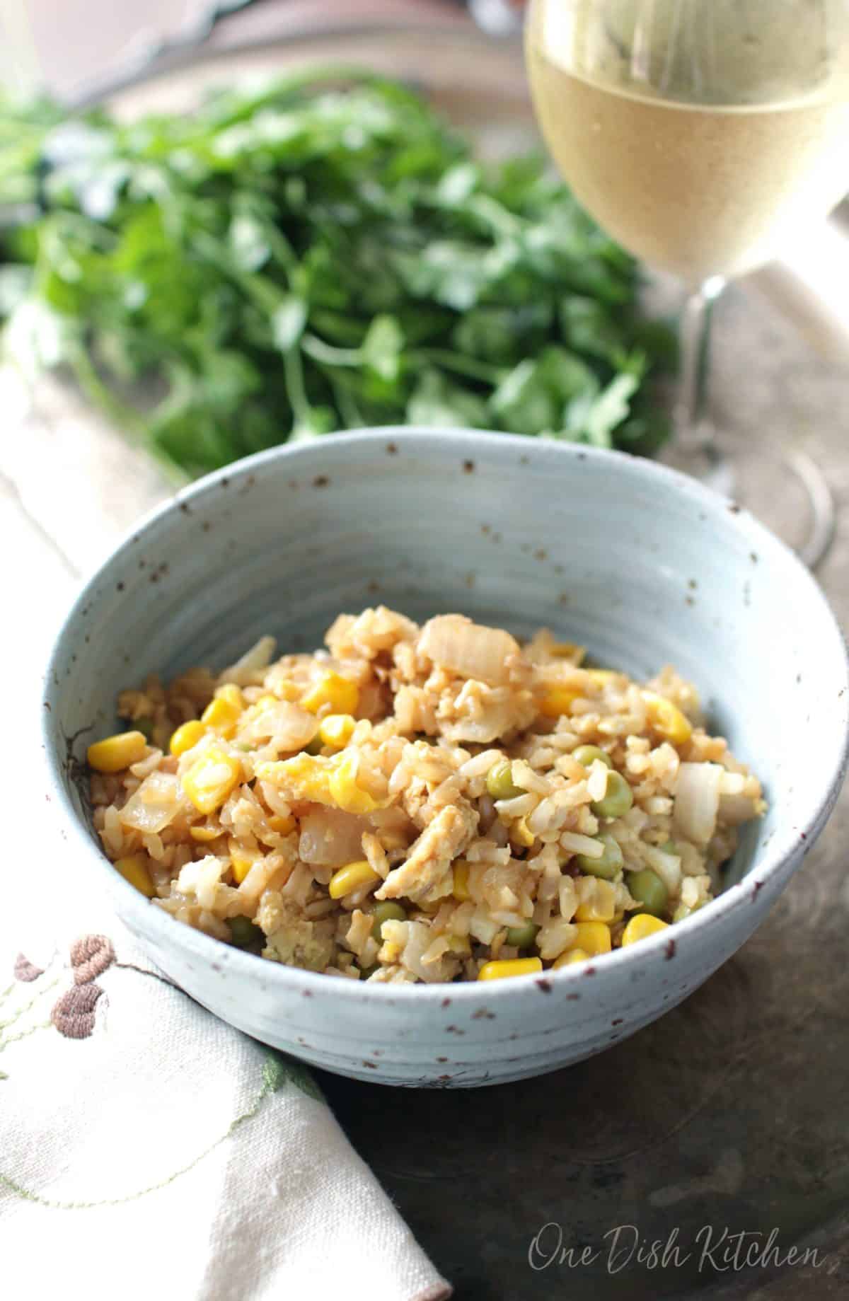 a blue bowl filled with fried rice, corn and peas next to a bunch of parsley.