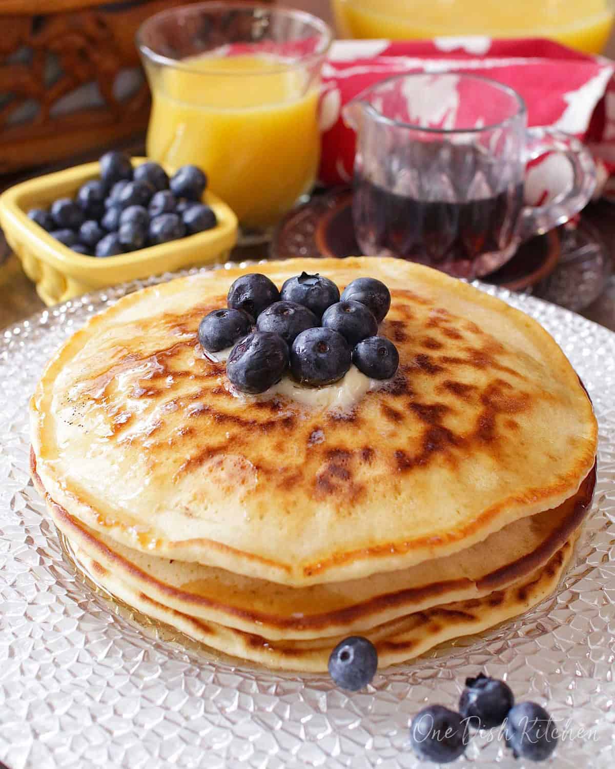 a short stack of pancakes on a plate topped with blueberries.