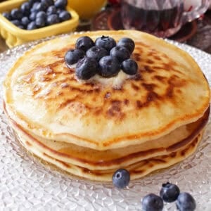 a short stack of pancakes on a plate topped with blueberries.