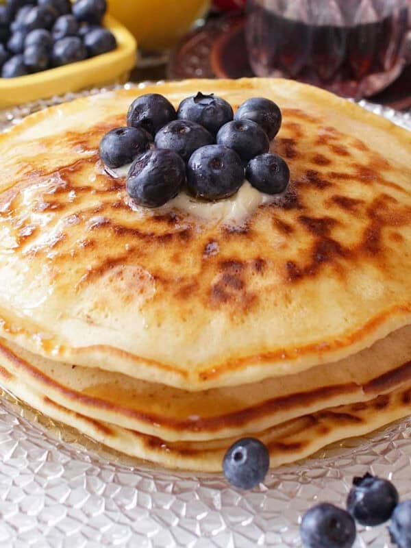 a short stack of pancakes on a plate topped with blueberries.