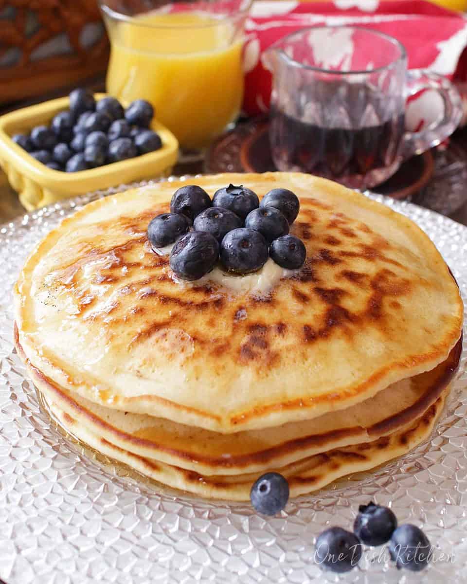 a short stack of pancakes on a plate topped with blueberries.