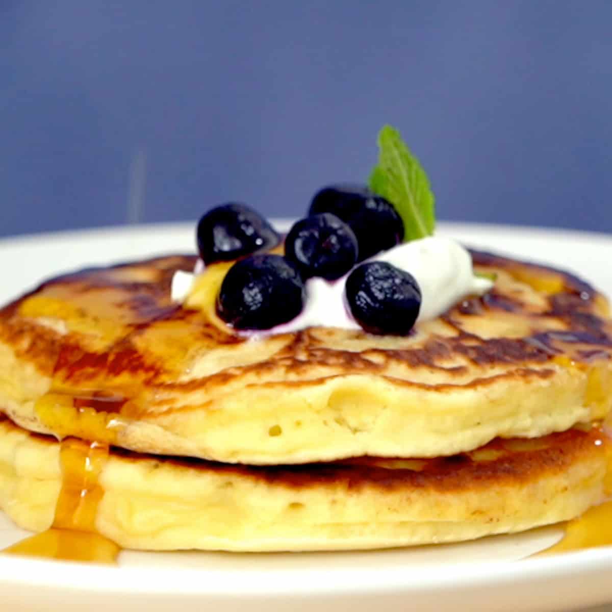 two pancakes on a plate topped with blueberries, butter, and syrup.