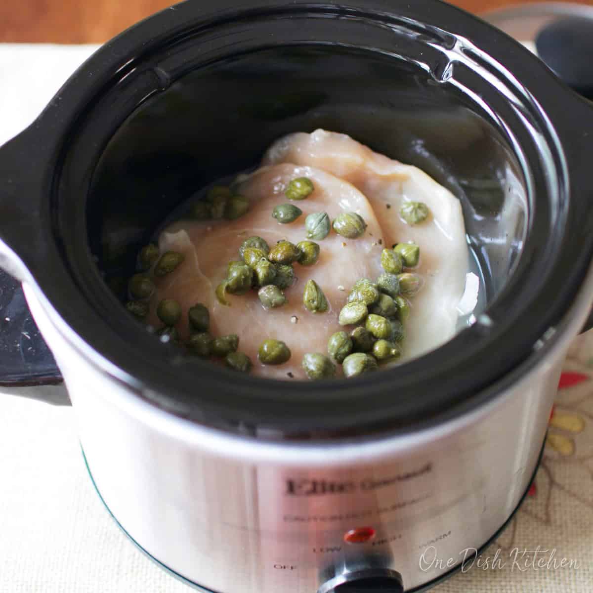 uncooked chicken piccata in a small slow cooker.