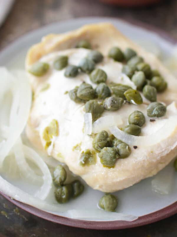 a chicken breast topped with slices of white onions and capers on a blue plate.