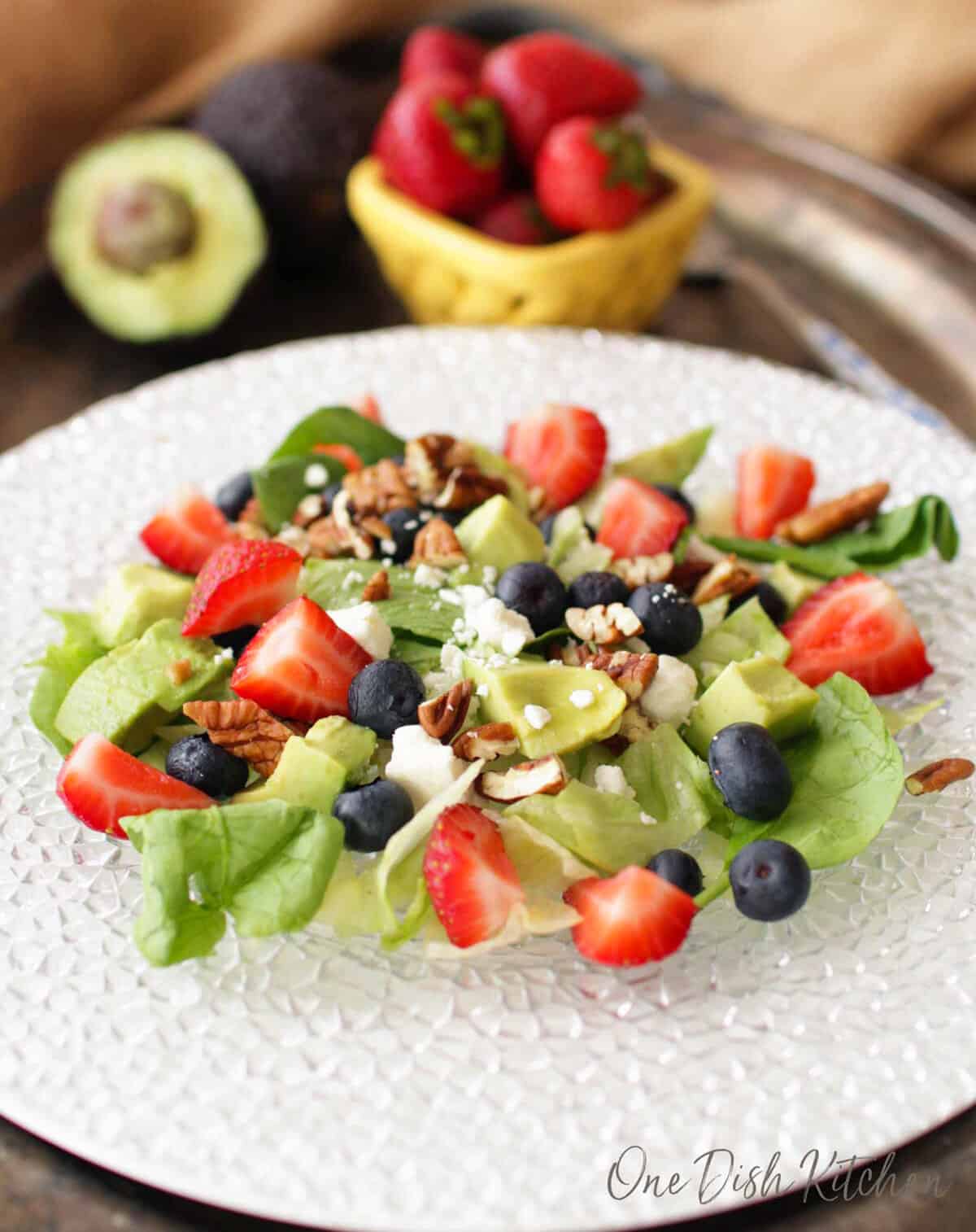 an avocado salad on a plate topped with blueberries and strawberries.