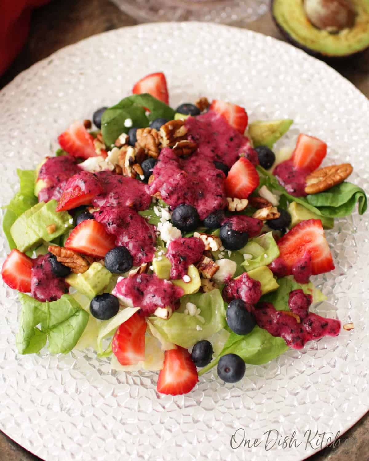 an avocado salad with berries and nuts topped with a blueberry vinaigrette.