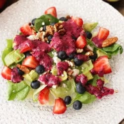 an avocado salad with berries and nuts topped with a blueberry vinaigrette.