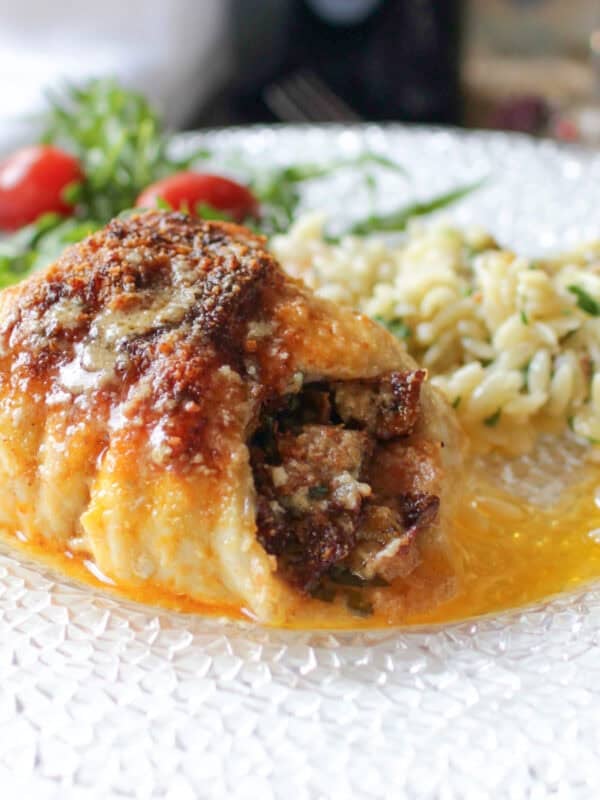 Single serving baked stuffed fish rolled and baked in a small dish, filled with bacon and vegetable stuffing and topped with Parmesan cheese, ready to serve.