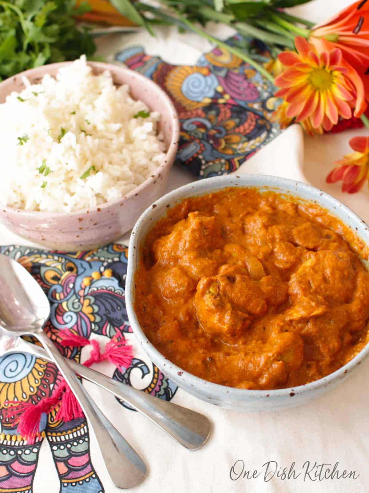 a blue bowl filled with butter chicken next to a bowl of white rice
