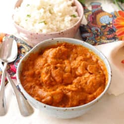 a blue bowl filled with butter chicken next to a pink bowl filled with white rice