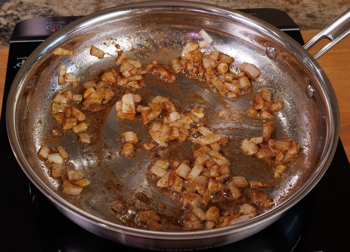onions and garlic cooking in garam masala, cumin, and turmeric in a skillet