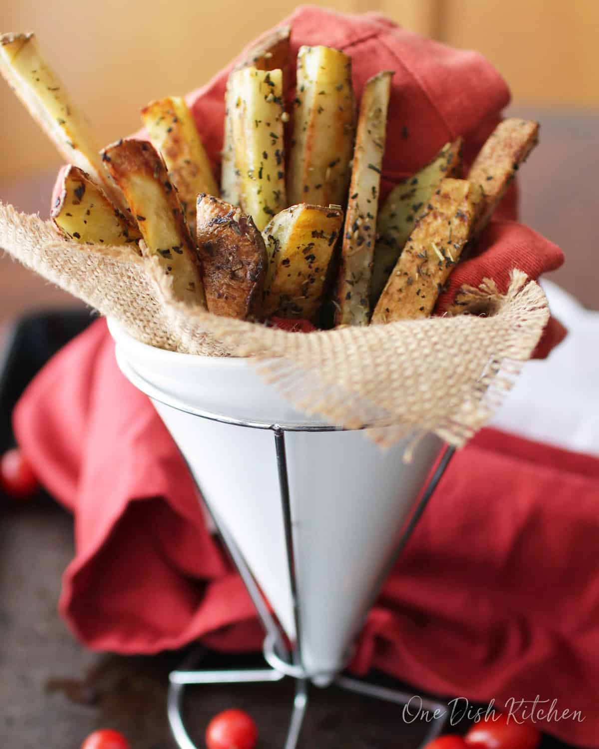 Seasoned french fries in a tall dish held together by a red cloth napkin and a burlap napkin.