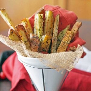 french fries cover with spices wrapped in white paper cone and in a stand.