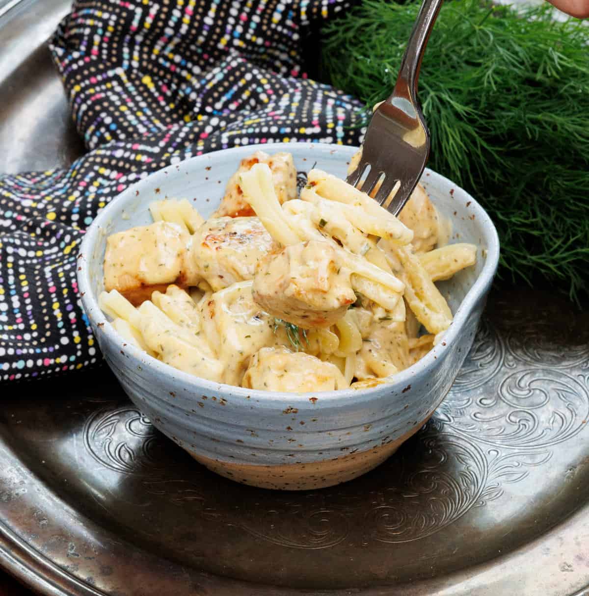 a fork filled with pasta and chicken over a blue bowl.