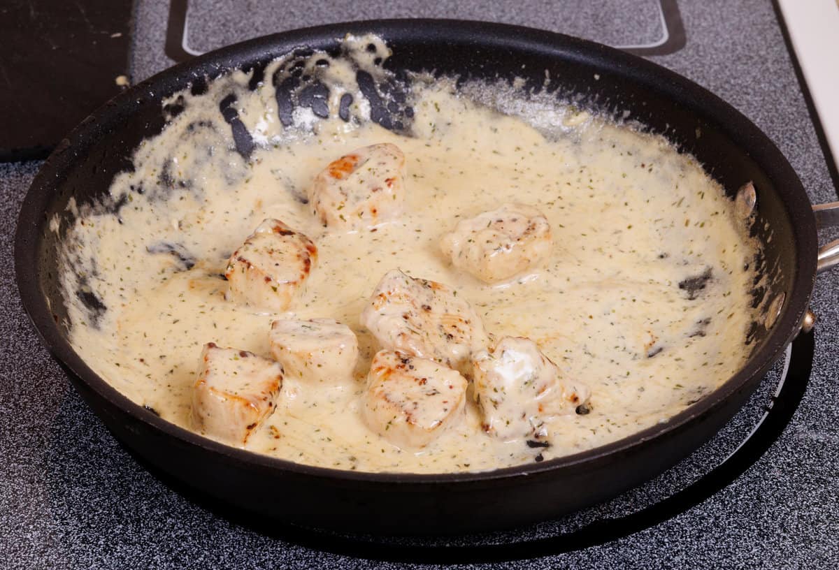 chicken with mustard tarragon sauce simmering in a saucepan.