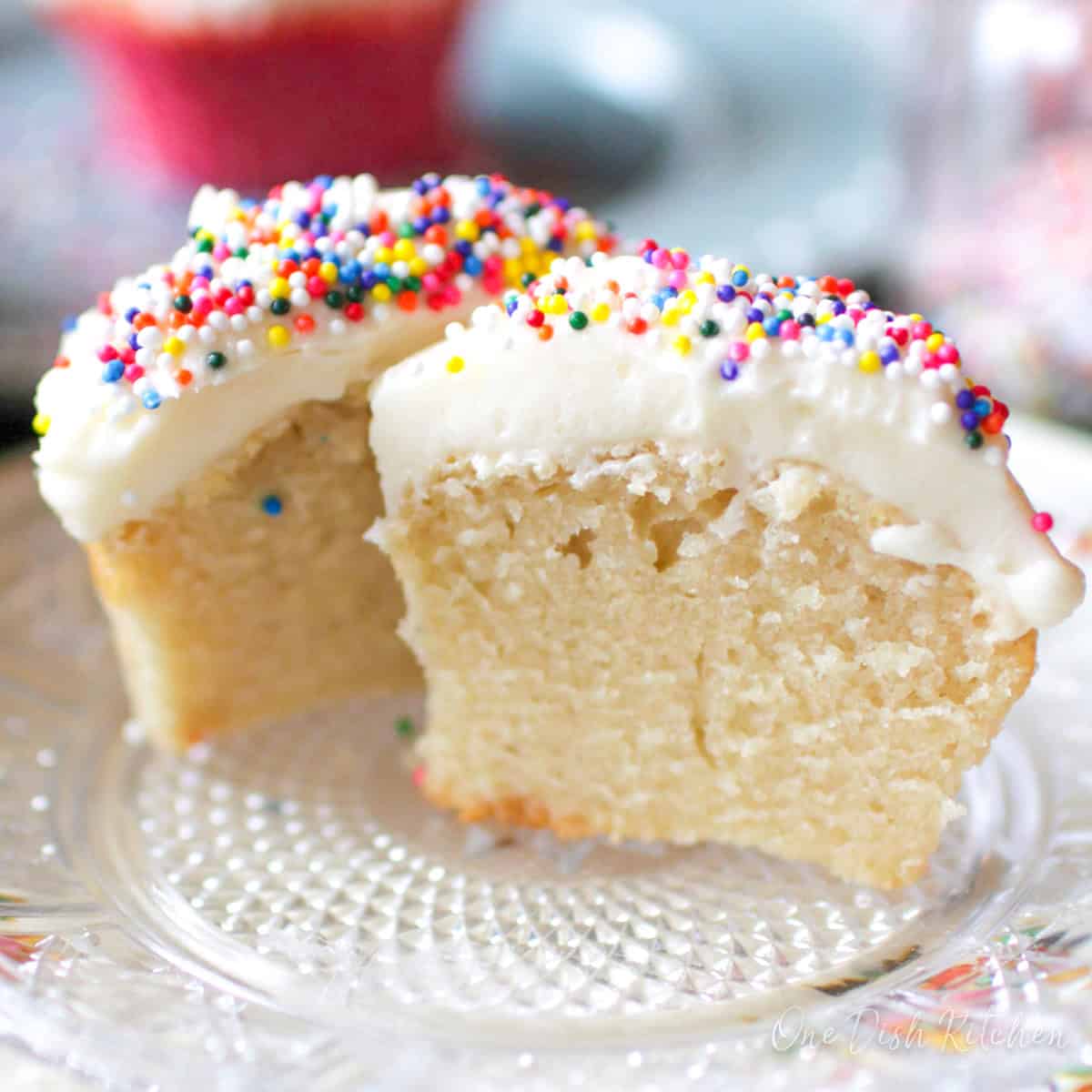one vanilla cupcake topped with vanilla frosting and candy sprinkles sliced in half.