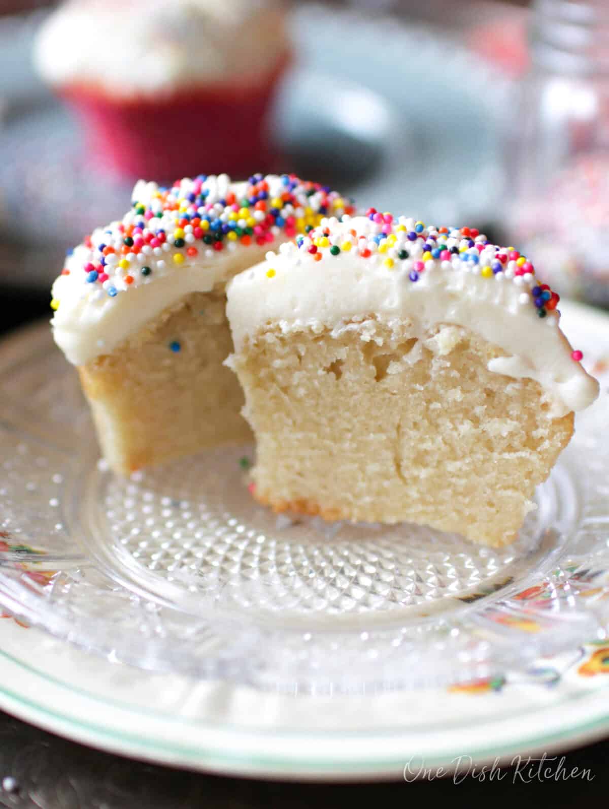 a vanilla cupcake sliced in half on a white plate.