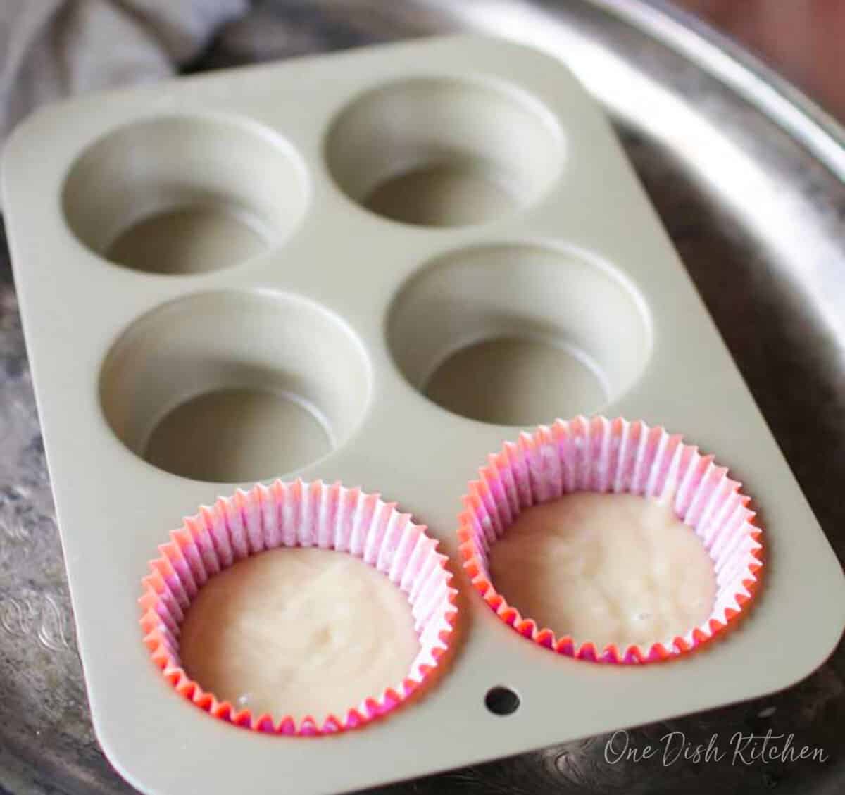two unbaked vanilla cupcakes in a muffin pan.