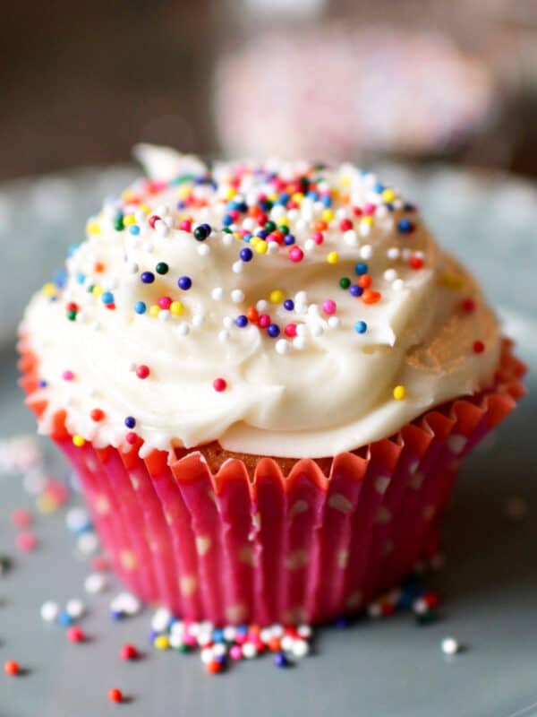 one vanilla cupcake topped with buttercream frosting and sprinkles on a green plate.