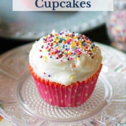 two vanilla cupcakes topped with sprinkles on plates.