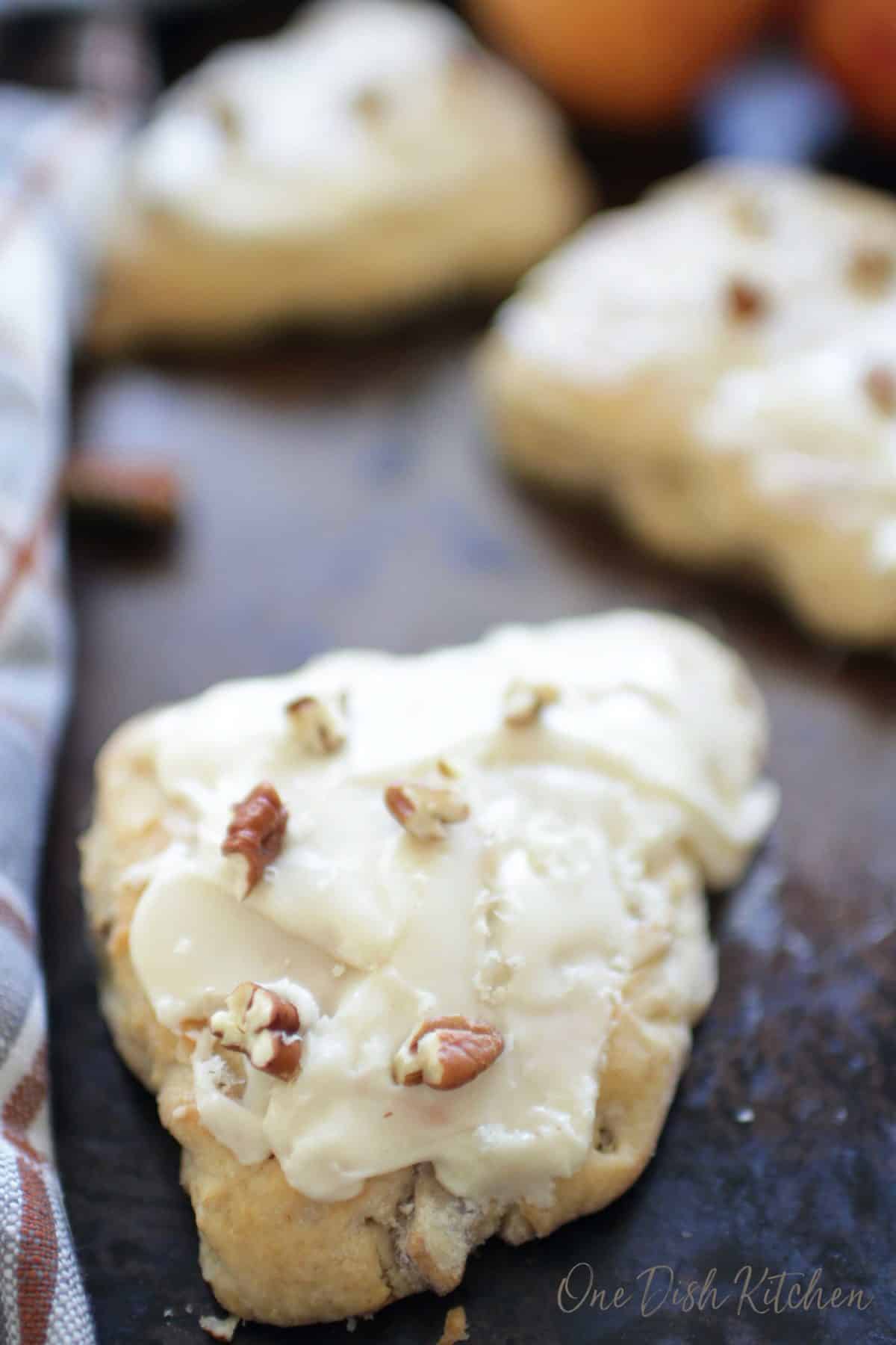 Three apple cinnamon scones on a baking sheet topped with white glaze and chopped pecans.