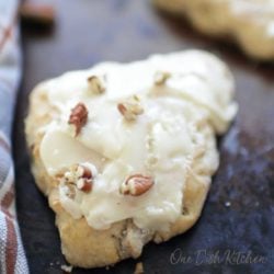 an apple cinnamon scone topped with a glaze and chopped pecans on a baking sheet