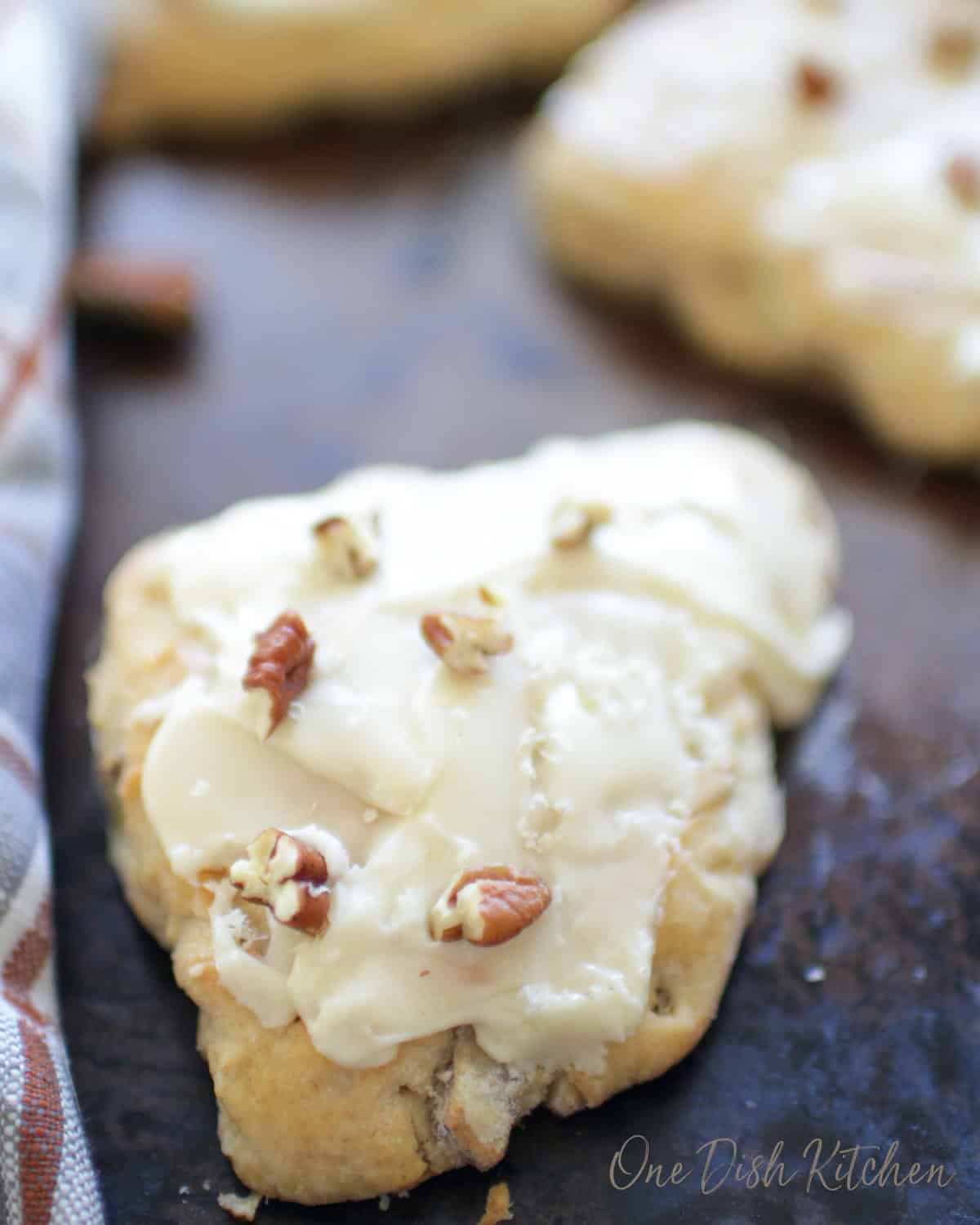 Three apple cinnamon scones on a baking sheet topped with white glaze and chopped pecans.