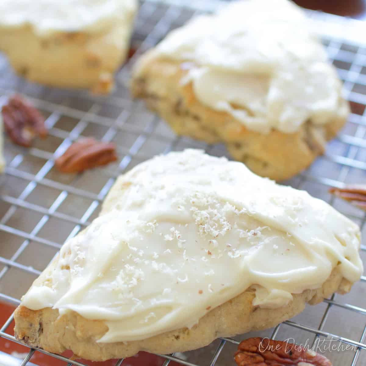 three frosted apple scones on a cooling rack.
