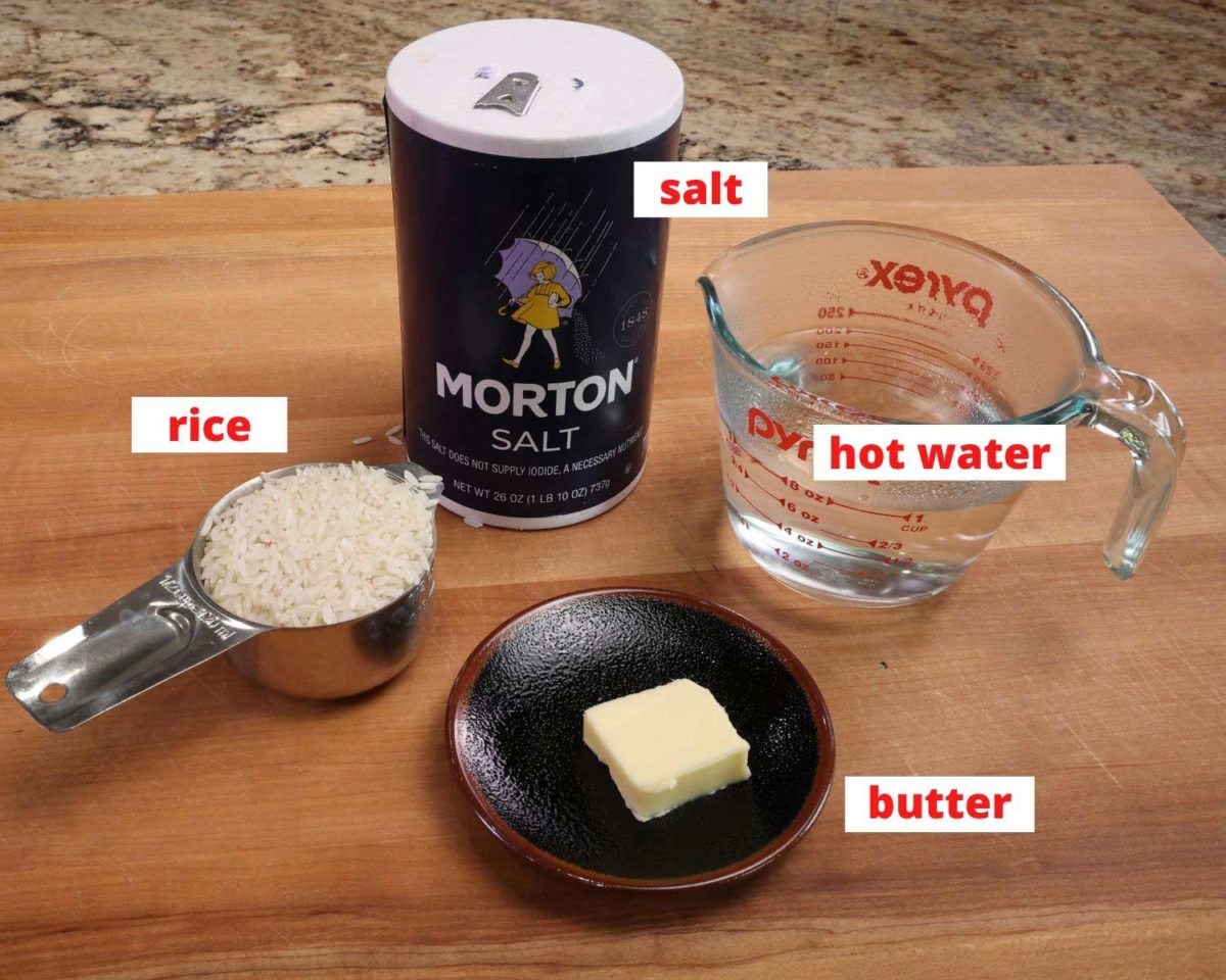 rice, salt, butter and a cup filled with water on a wooden cutting board.