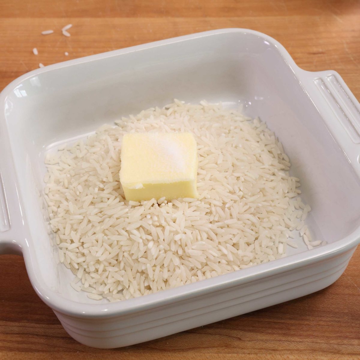 a white square bowl with rice and butter inside.