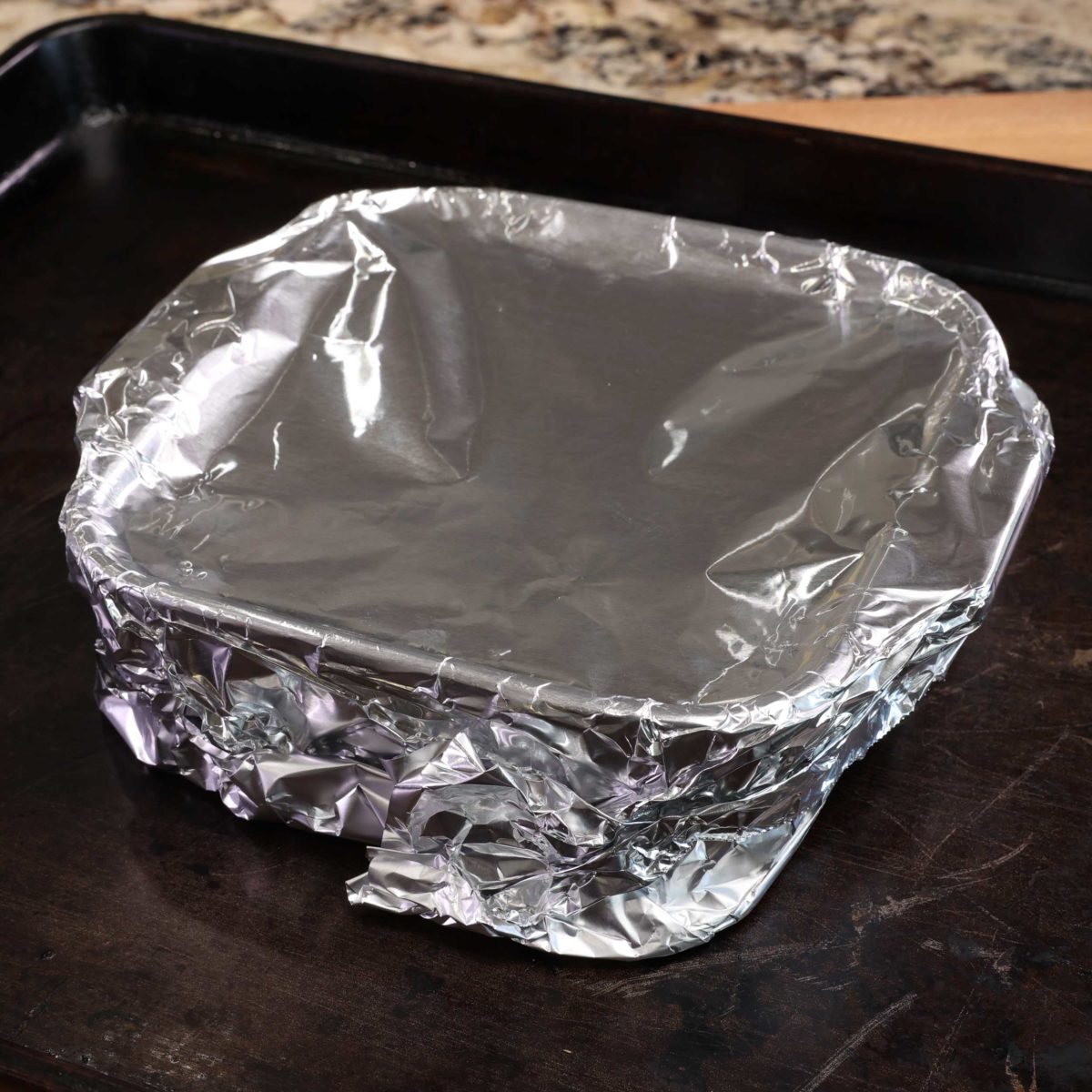 aluminum foil covering a small square baking dish on a baking sheet.