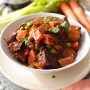 a bowl of beef stew next to carrots and celery on a silver tray