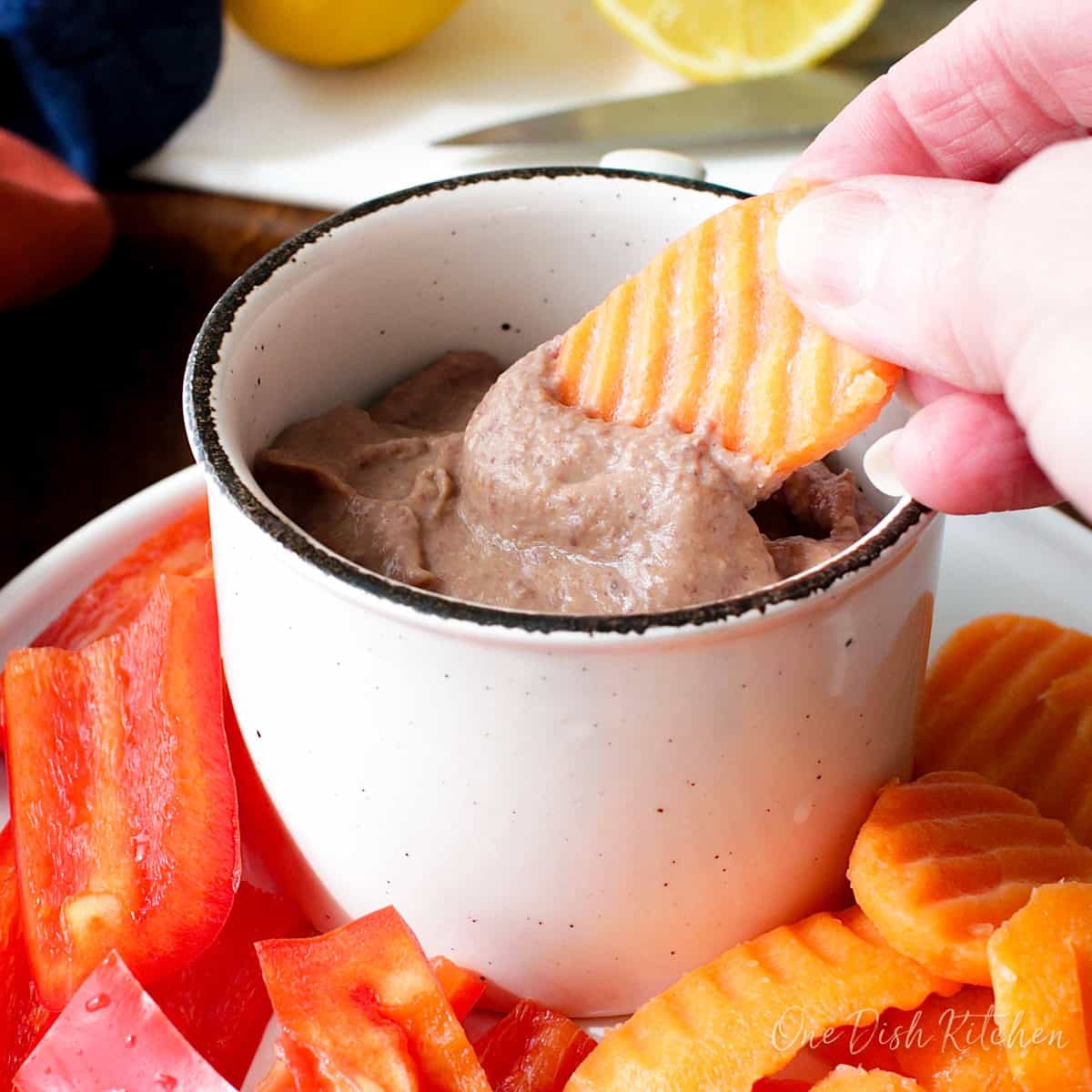 a small batch of black bean hummus in a bowl surrounded by sliced vegetables for dipping.