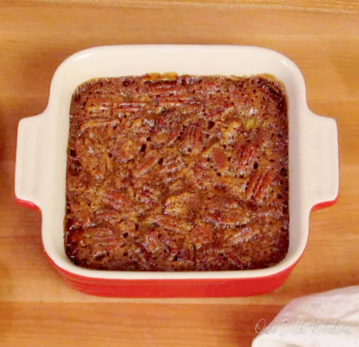 a mini pecan pie in a red square baking dish.