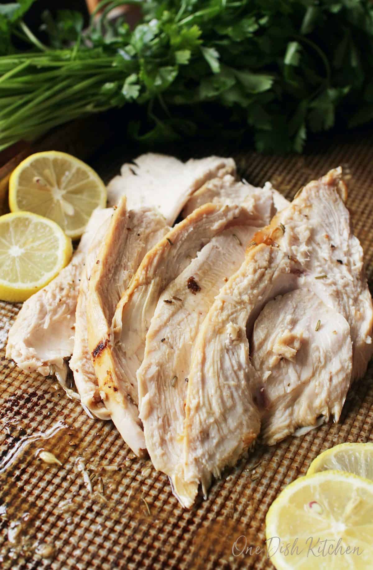 Sliced roasted turkey breast on a baking dish with four lemon wheels 