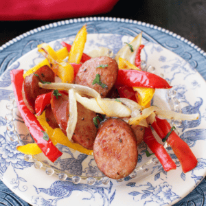 Sliced roasted sausage, red and yellow peppers, and onions on a plate.