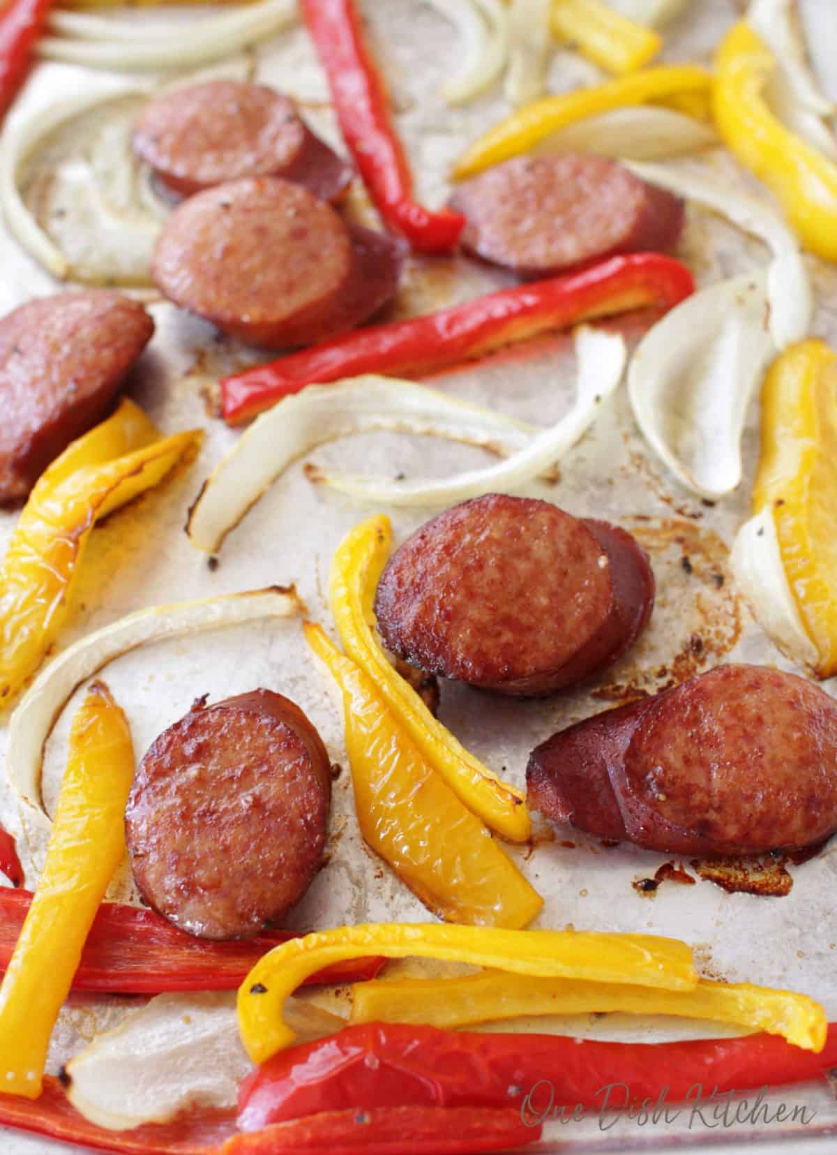 sausage, peppers, and sliced onions scattered on a baking sheet.