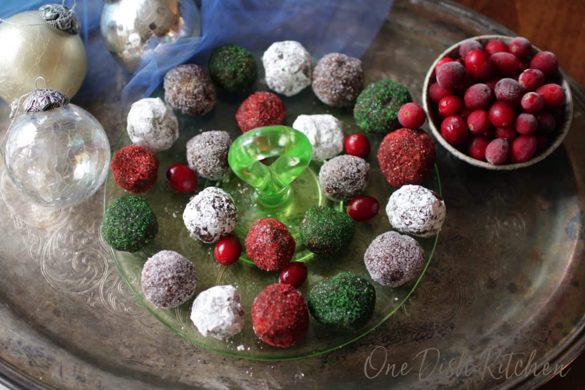 an overhead picture of a plate of red, green and white sugar plums surrounded by fresh cranberries and silver christmas ornaments.