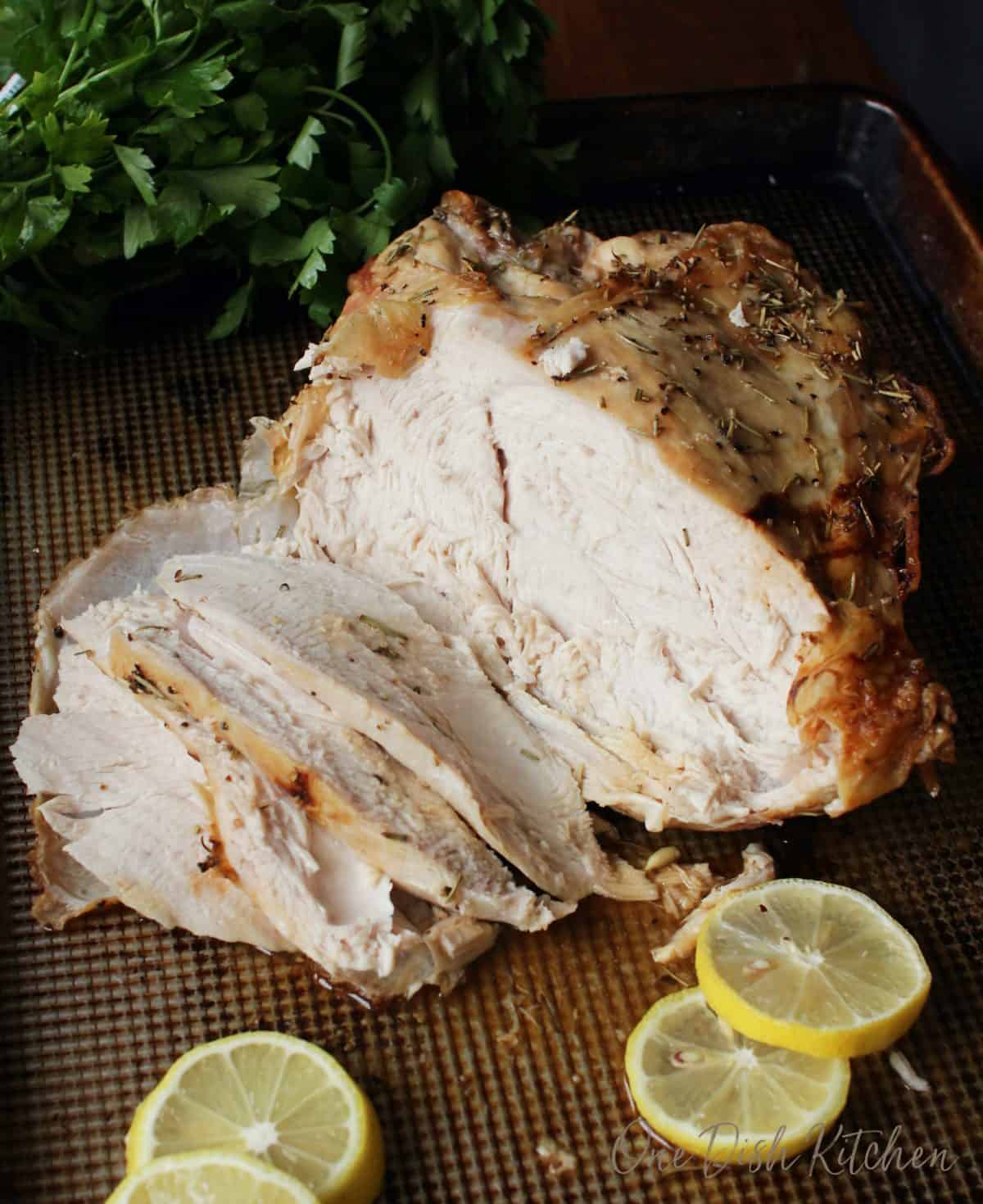 Roast turkey breast cut into slices on a baking dish with four lemon wheels