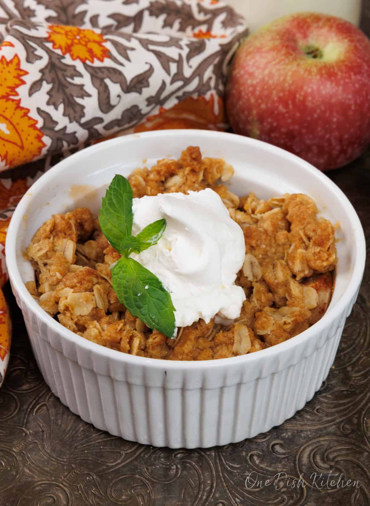 one small apple crisp in a white ramekin on a silver tray.