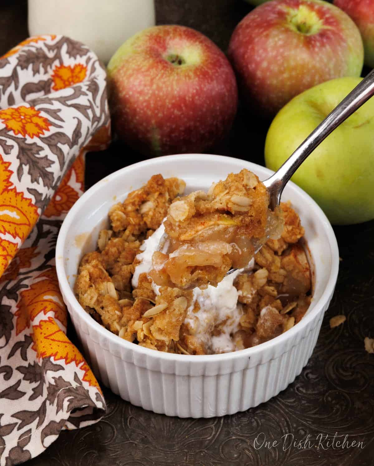 a spoon in an individual apple crisp with apples hanging off of the spoon