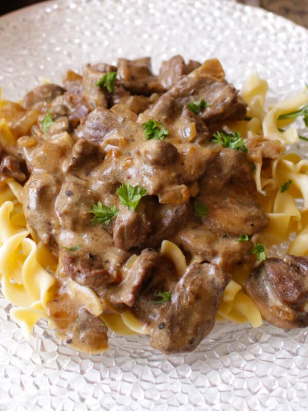 a white plate filled with noodles and beef stroganoff.