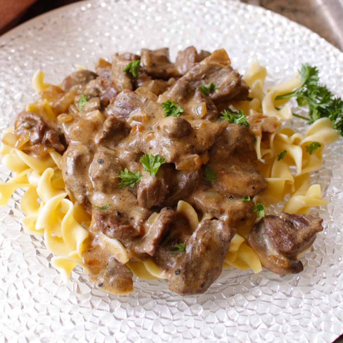 a white plate filled with noodles and beef stroganoff.