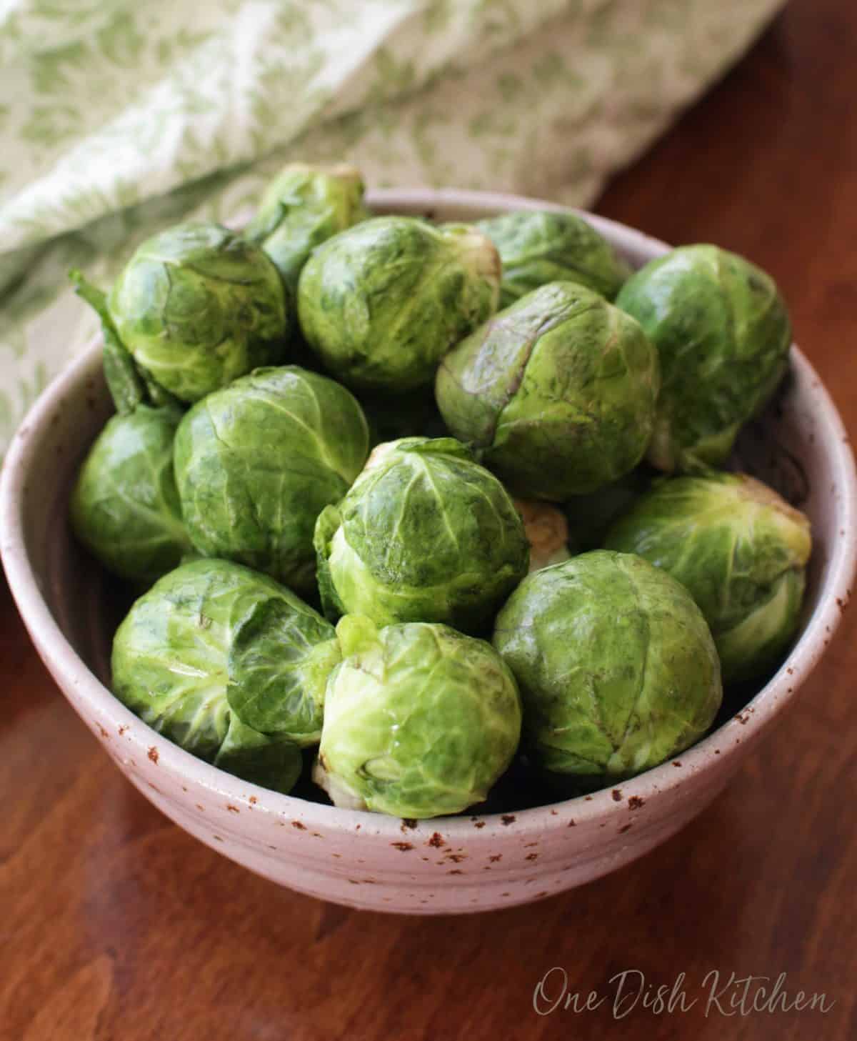 a pink bowl filled with raw brussels sprouts.