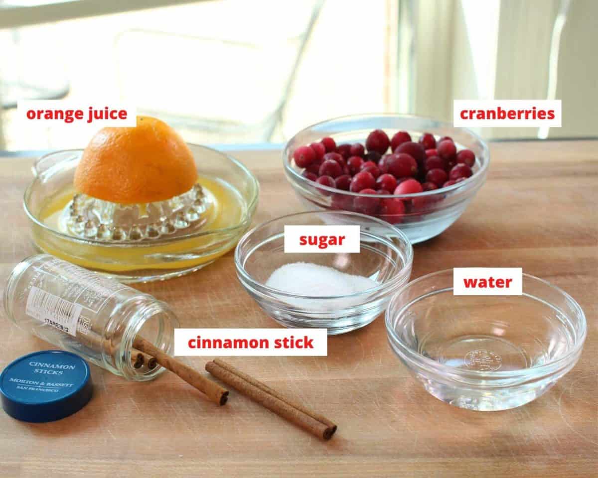 the ingredients to make cranberry sauce labeled and on a brown table.