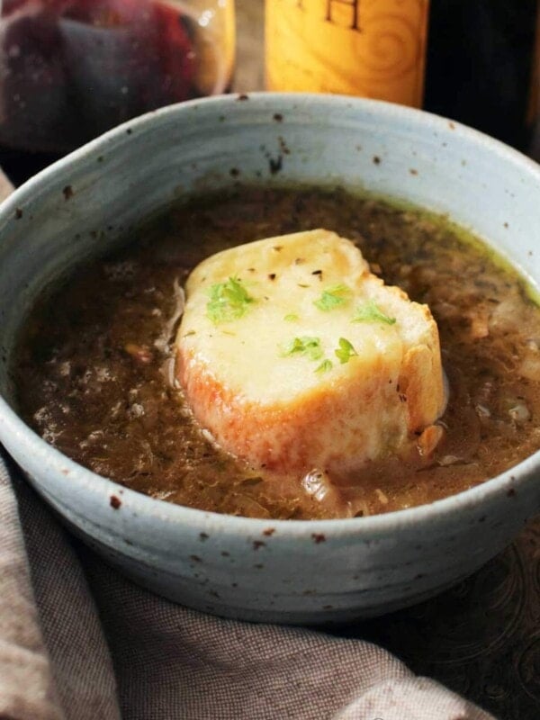 a blue bowl filled with french onion soup with a piece of french bread topped with melted cheese floating on top